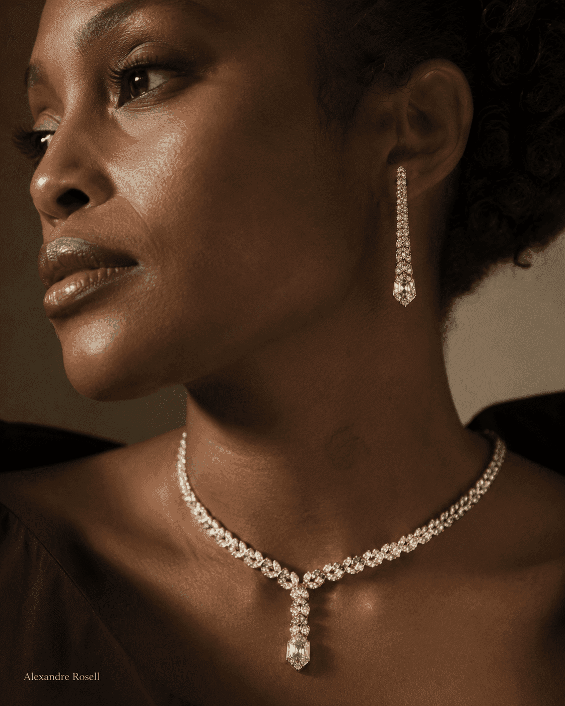 A woman in a diamond riviere and drop earrings under soft editorial light.