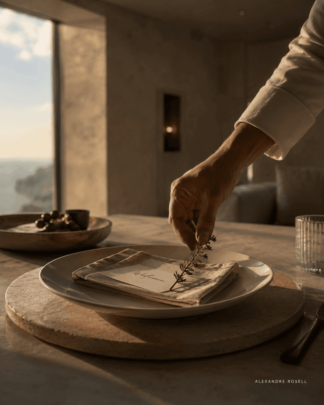 A hand laying a sprig of rosemary onto a plated course in a stone-walled room above the sea.